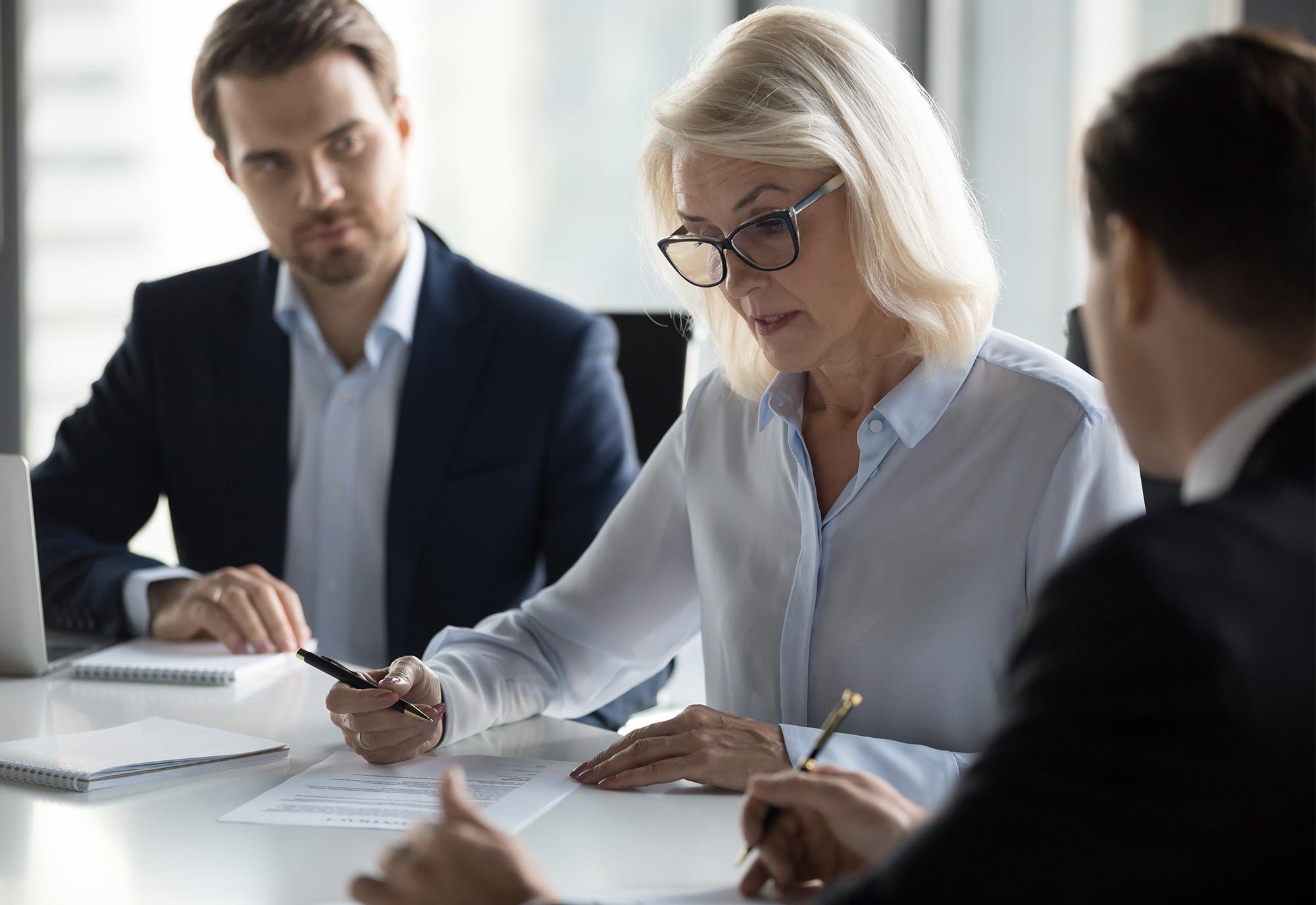 woman sits between two men in an office boardroom reading paper documents