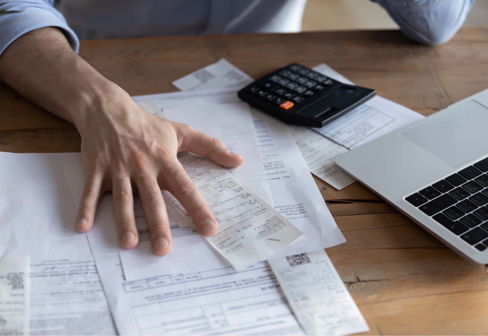 man sits at table reading through paperwork with laptop and calculator