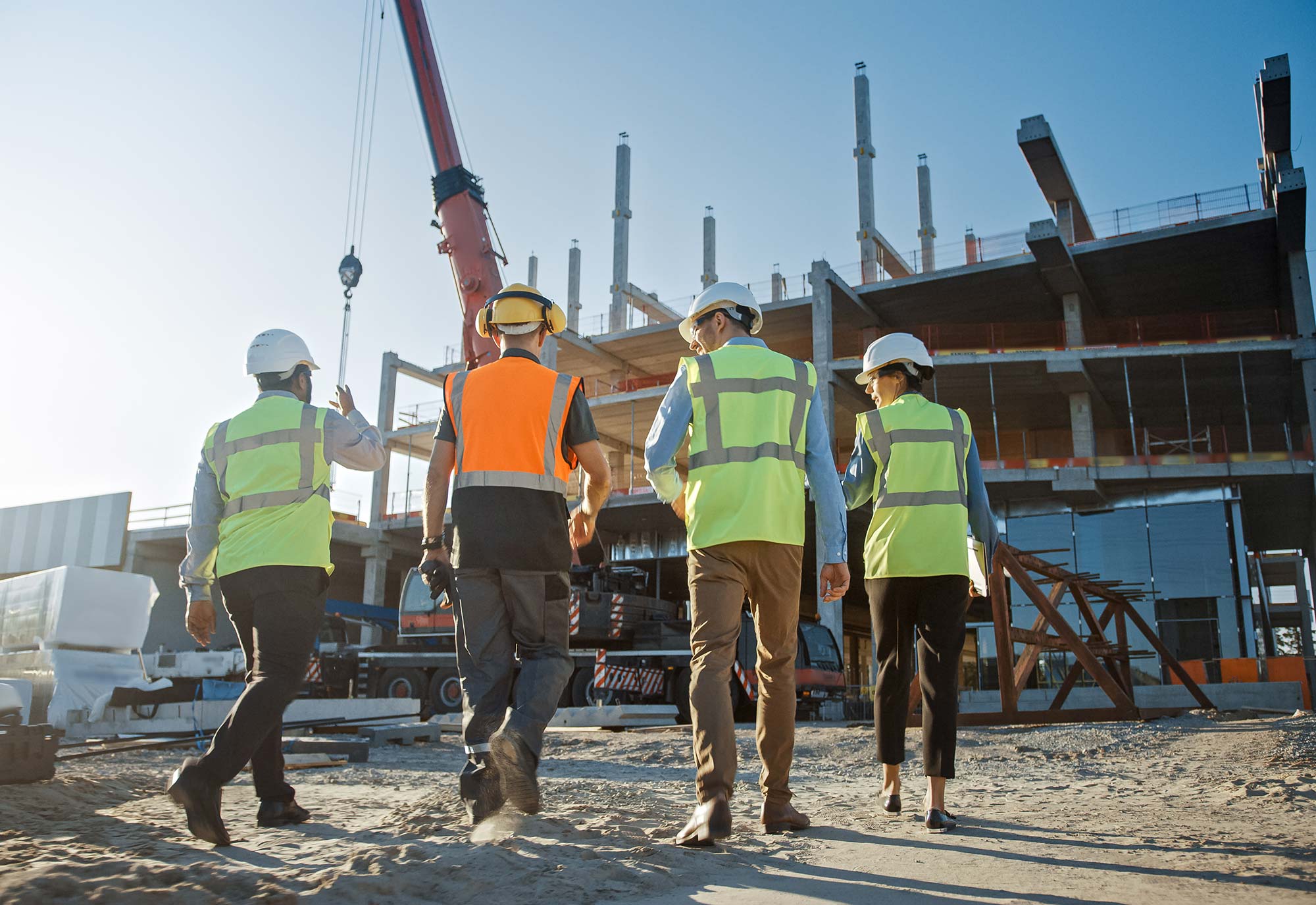 Three men and a women wearing high visability jackets and hard hats walk up to a construction site