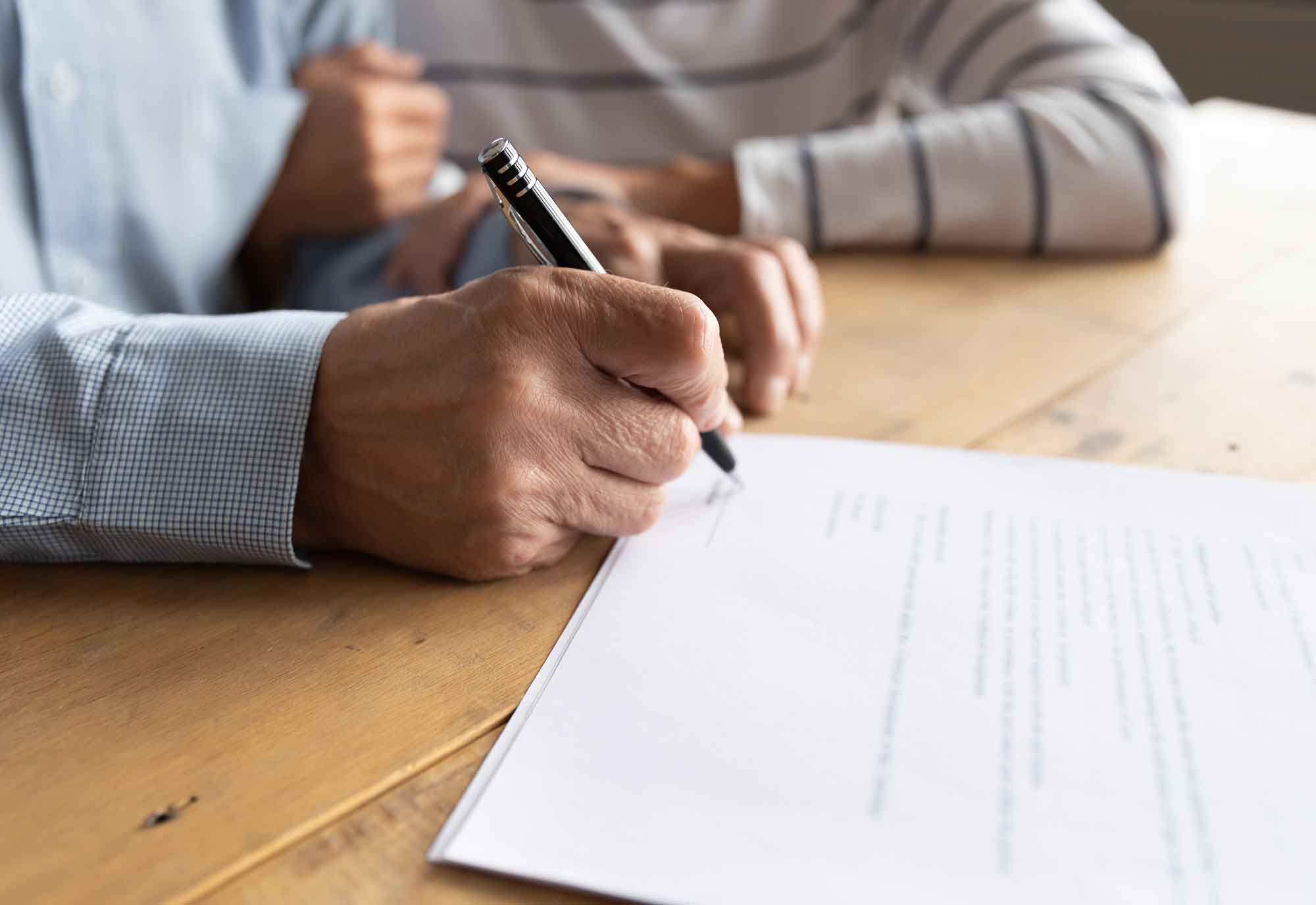 close up of older couple sitting at their dinning room table as the man holds a pen ready to sign a document