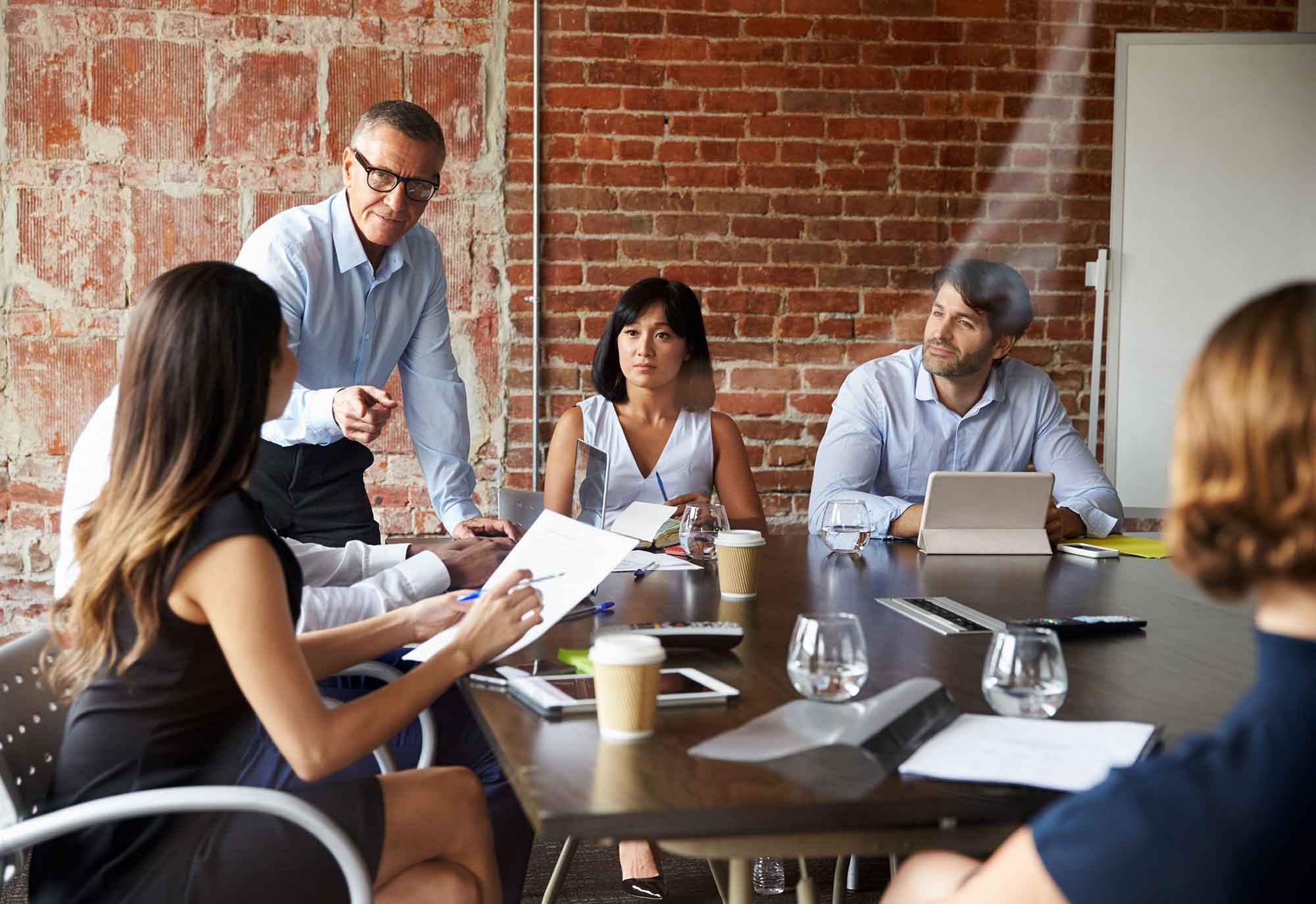 mixed group of male and female businesses workers communicate while sitting round a boardroom table in a modern office