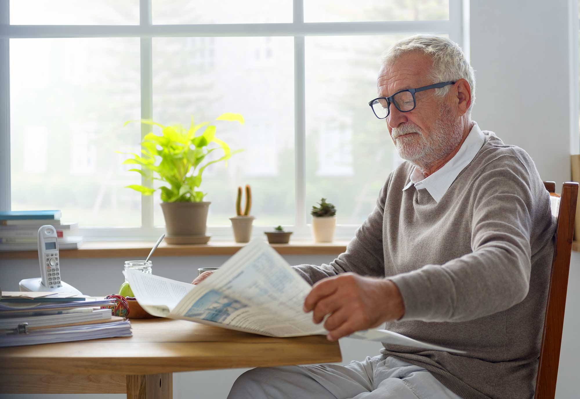 Elderly man reading newspaper at a table